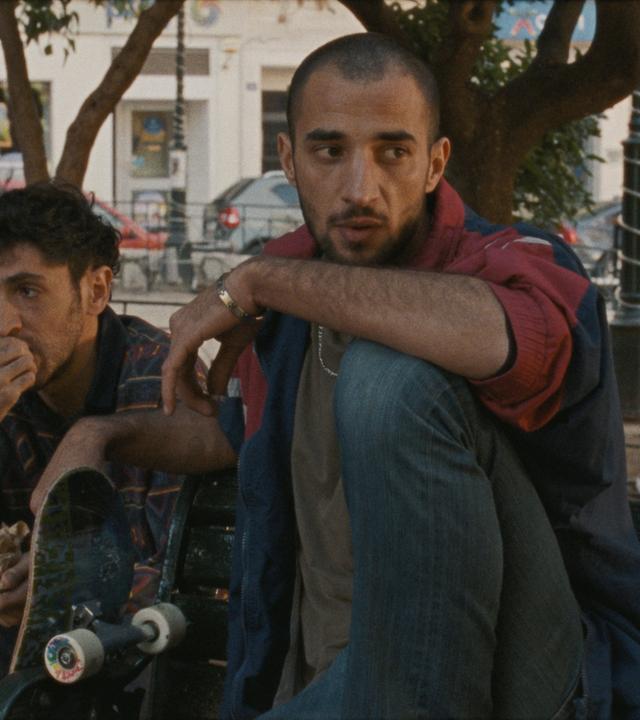 Zwei Männer sitzen unter Bäumen in einer Stadt.