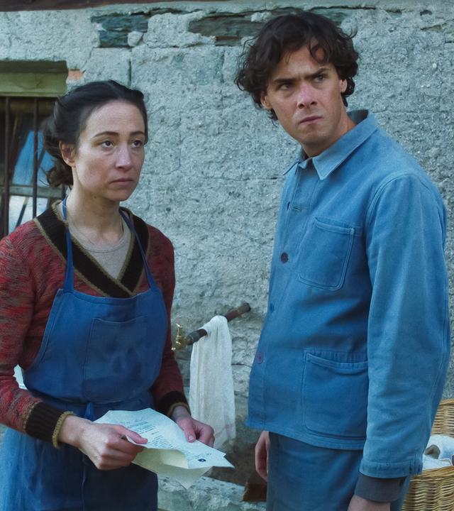 Eine Frau und ein Mann stehen vor einem alten Steinhaus.