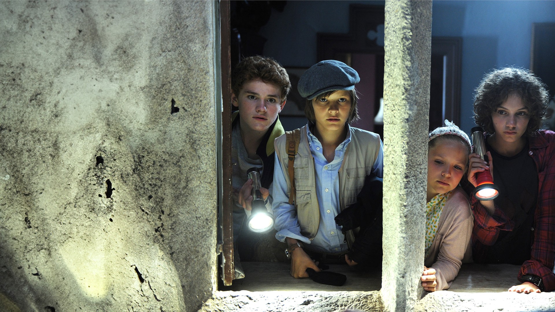 Von links nach rechts: Die "Fünf Freunde" tappen im Dunkeln mit Taschenlampen in der Hand. Julian (Quirin Oettl), Anne (Neele Marie Nickel), Dick (Justus Schlingensiepen) und George (Valeria Eisenbart). Vor ihnen ein dichtes Netz aus Spinnenweben. 