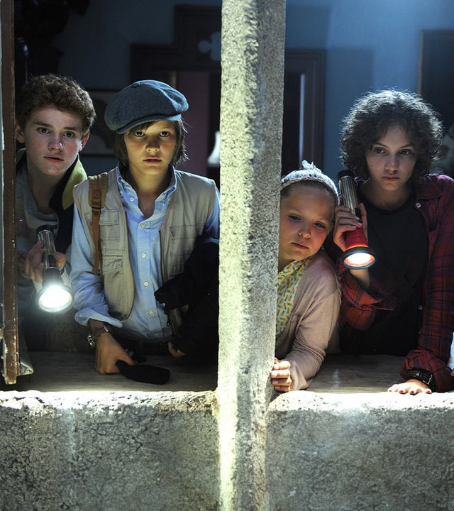 Von links nach rechts: Die "Fünf Freunde" tappen im Dunkeln mit Taschenlampen in der Hand. Julian (Quirin Oettl), Anne (Neele Marie Nickel), Dick (Justus Schlingensiepen) und George (Valeria Eisenbart). Vor ihnen ein dichtes Netz aus Spinnenweben. 