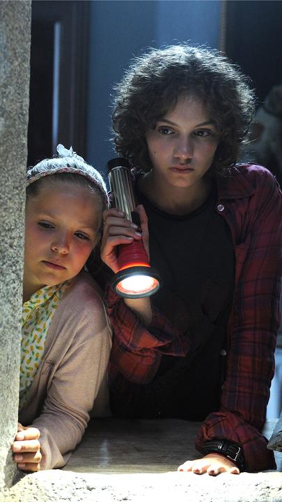 Von links nach rechts: Die "Fünf Freunde" tappen im Dunkeln mit Taschenlampen in der Hand. Julian (Quirin Oettl), Anne (Neele Marie Nickel), Dick (Justus Schlingensiepen) und George (Valeria Eisenbart). Vor ihnen ein dichtes Netz aus Spinnenweben. 