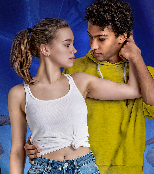 Katya (links; Alexandra Pfeifer) und Marlon (rechts; Yalany Marschner) stehen vor blauem Hintergrund beieinander. Beide schauen sich tief in die Augen. Im Hintergrund (links) steht Marlon (klein) in Hip-Hop-Pose; (rechts) tanzt Katya (klein) im Tutu in Ballettpose.
