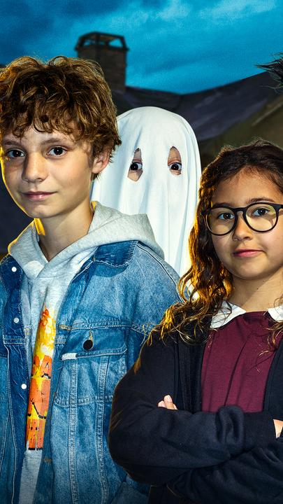 Vier Kinder, eines als Werwolf und eines als Gespenst verkleidet, sind im Vordergrund zu sehen. Es ist dunkel. Im Hintergrund steht ein gruselig beleuchtetes Haus.