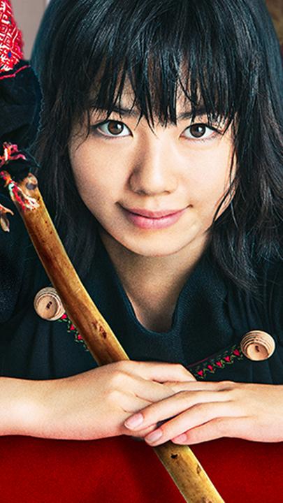 Kiki steht im Ladenraum der Bäckerei. Ihren magischen Besen hat sie in den Händen, eine schwarze Katze blickt über ihre Schulter.