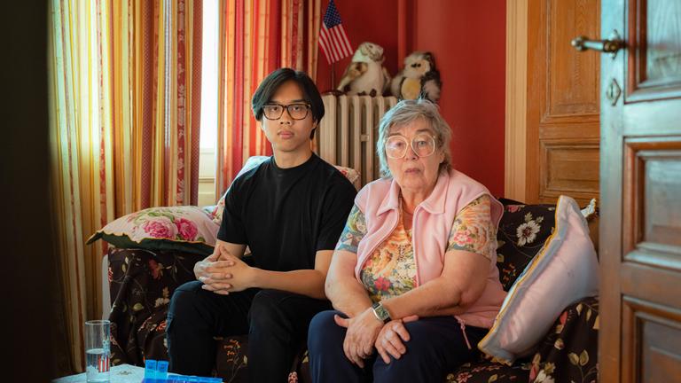 Szene aus "Der Kaiser der Freude" von Ocean Vuong: Ein junger vietnamesicher Mann und eine alte Frau sitzen auf einem geblümten Sofa.