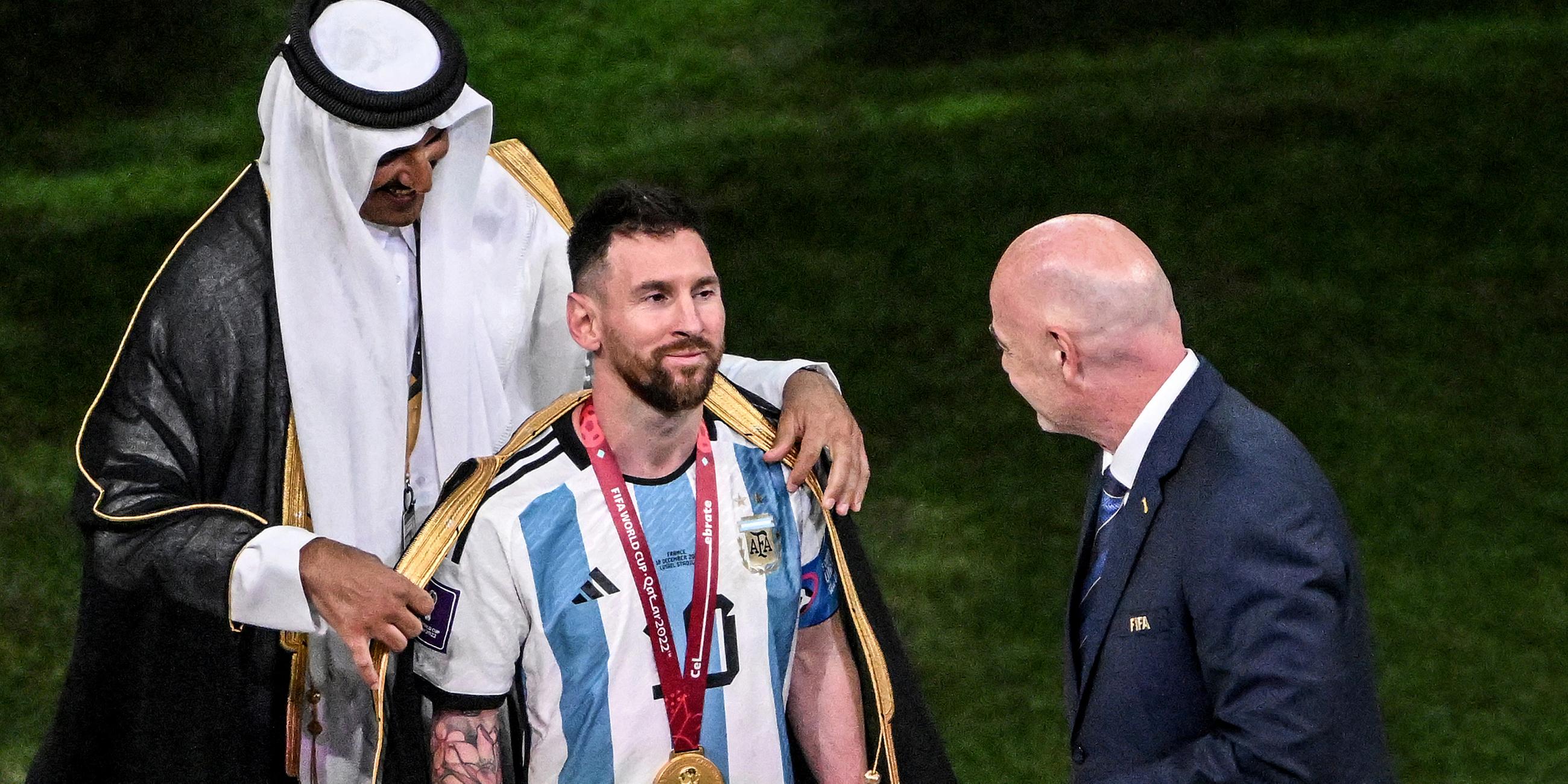 Emir von Katar, Scheich Tamim bin Hamad Al Thani, legt Argentiniens Lionel Messi vor Übergabe des WM-Pokals vor Fifa-Präsident Gianni Infantino ein Bischt, ein traditionelles arabische Kleidungsstück an.