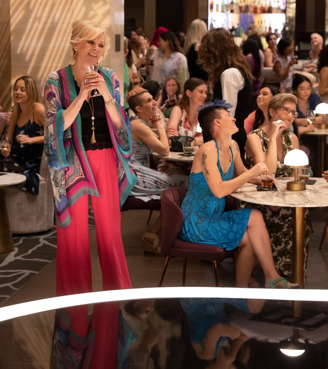 "Hacks - Findet mich toll, einfach": Deborah (Jean Smart) steht lächelnd mit einem Martini-Glas in der Hand, in einer gut besuchten Bar vor einer Bühne, während um sie herum weibliche Gäste an Tischen sitzen und sich unterhalten.
