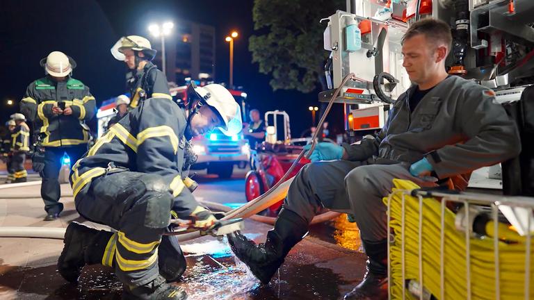 Ein Feuerwehrmann putzt einem anderen nach dem Einsatz die Schuhe