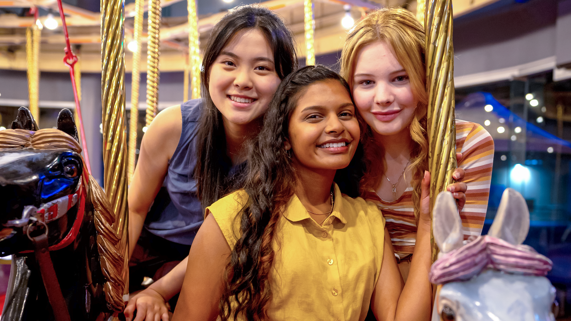 Olivia, Natalie und Hannah posieren für ein gemeinsames Foto auf einem Drehkarussell. Dabei sitzen sie auf Pferdefiguren des Fahrgeschäfts.