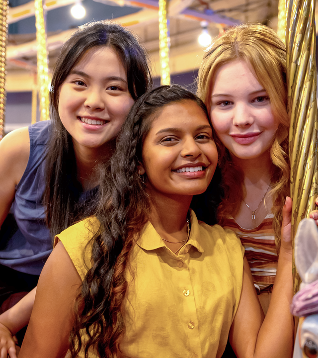 Olivia, Natalie und Hannah posieren für ein gemeinsames Foto auf einem Drehkarussell. Dabei sitzen sie auf Pferdefiguren des Fahrgeschäfts.