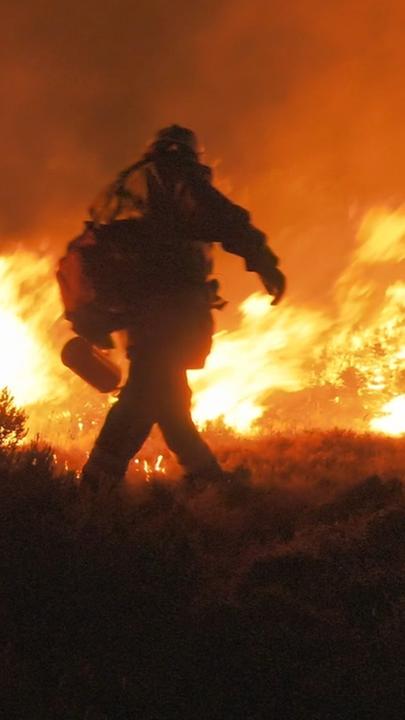"Flammendes Inferno - Feuerwehr hautnah: Wettlauf gegen die Zeit": Zwei Feuerwehrmänner versuchen mit Feuerlöschern, bei Nacht einen Waldbrand zu bekämpfen.