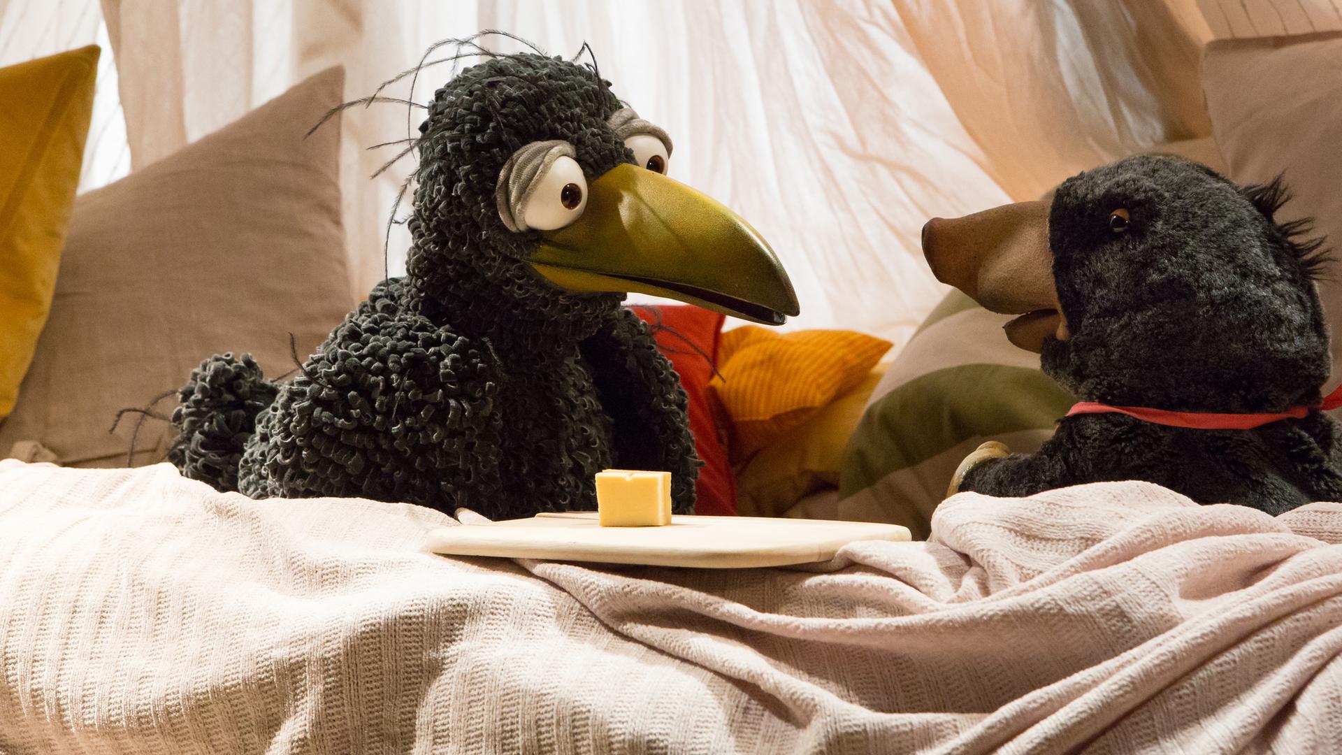 Rudi schaut neugierig auf Grete, die aufgeregt vor ihm in der Kuschelecke sitzt. Neben Grete steht ein Brettchen mit Käsehäppchen.