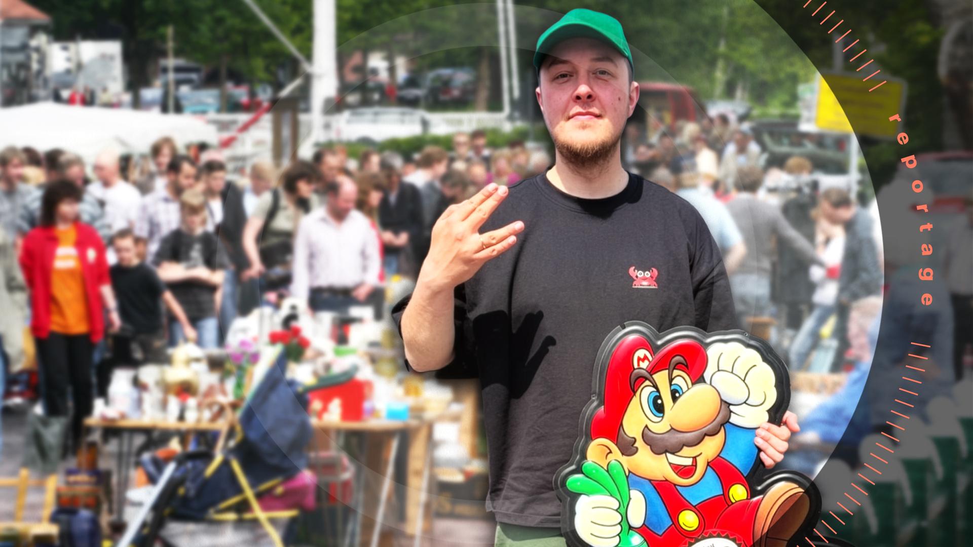 Jonas steht vor einem großen Auto und hält eine Wanddekoration von einer alten Videospielkonsole in der Hand.