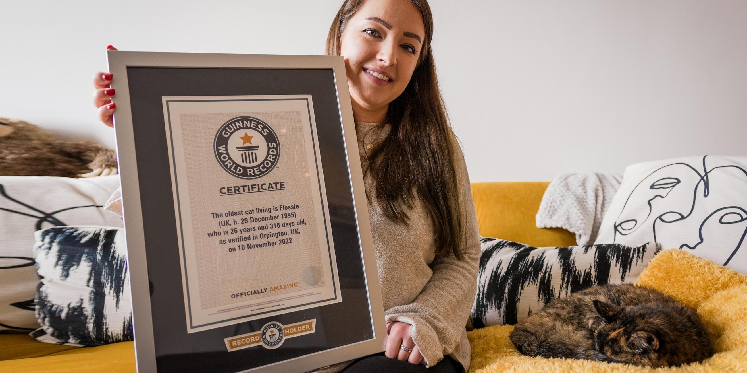 Die Katze Flossie und ihre Besitzerin Vicki Green sitzen mit der Urkunde der Guinness World Records auf einem Bett.
