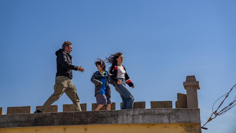 Tom (Hans Sigl), Noa (Santiago André) und Sophia (Hana Sofia Lopes) rennen über ein Hausdach. Dabei hält Sofia die Hand von Noa, der sich besorgt nach Tom umblickt.