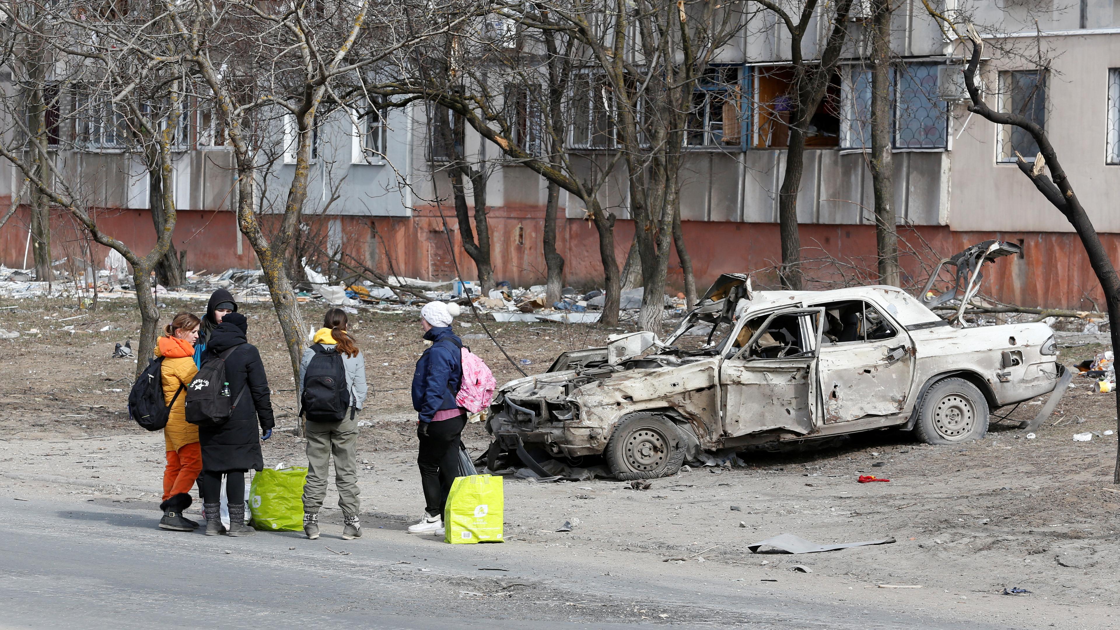 Fünf Menschen stehen vor einem zerstörten Auto in Mariupol.