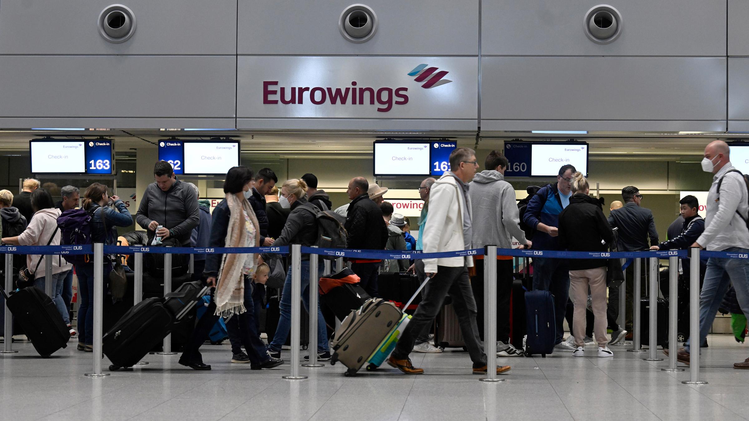 Reisende stehen am Eurowings Check-In-Schalter Schlange.
