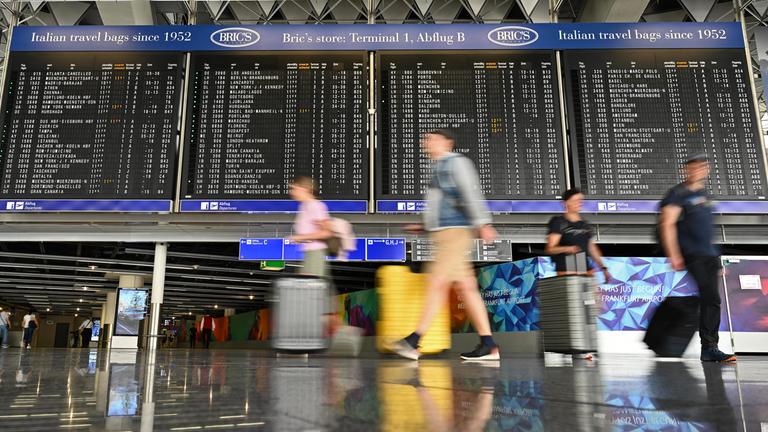 Urlauber laufen im Terminal 1 an einer großen Anzeigetafel vorbei. 