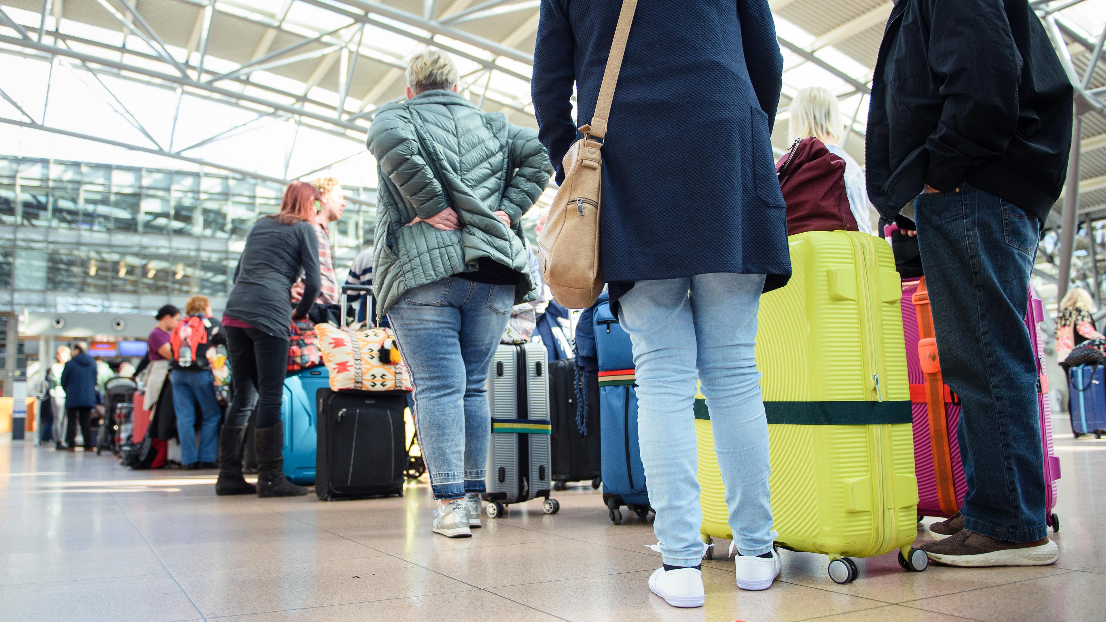Reisende stehen im Terminal des Flughafen Hamburg mit ihren Rollkoffern in einer Warteschlange an einem Check in-Schalter, aufgenommen am 24.04.2023