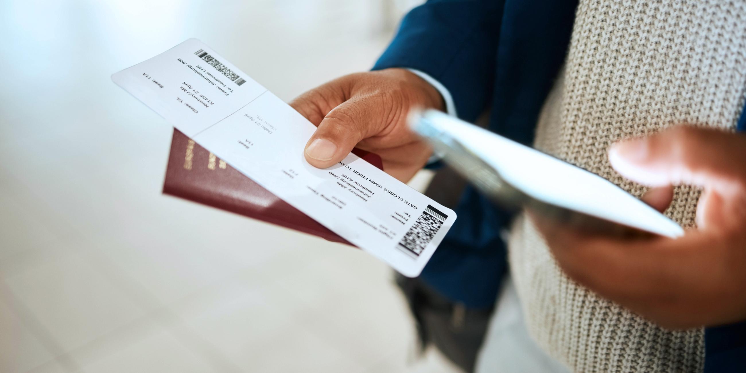 Mann hält sein Flugticket gemeinsam mit seinem Pass und einem Mobilfunkgerät in den Händen