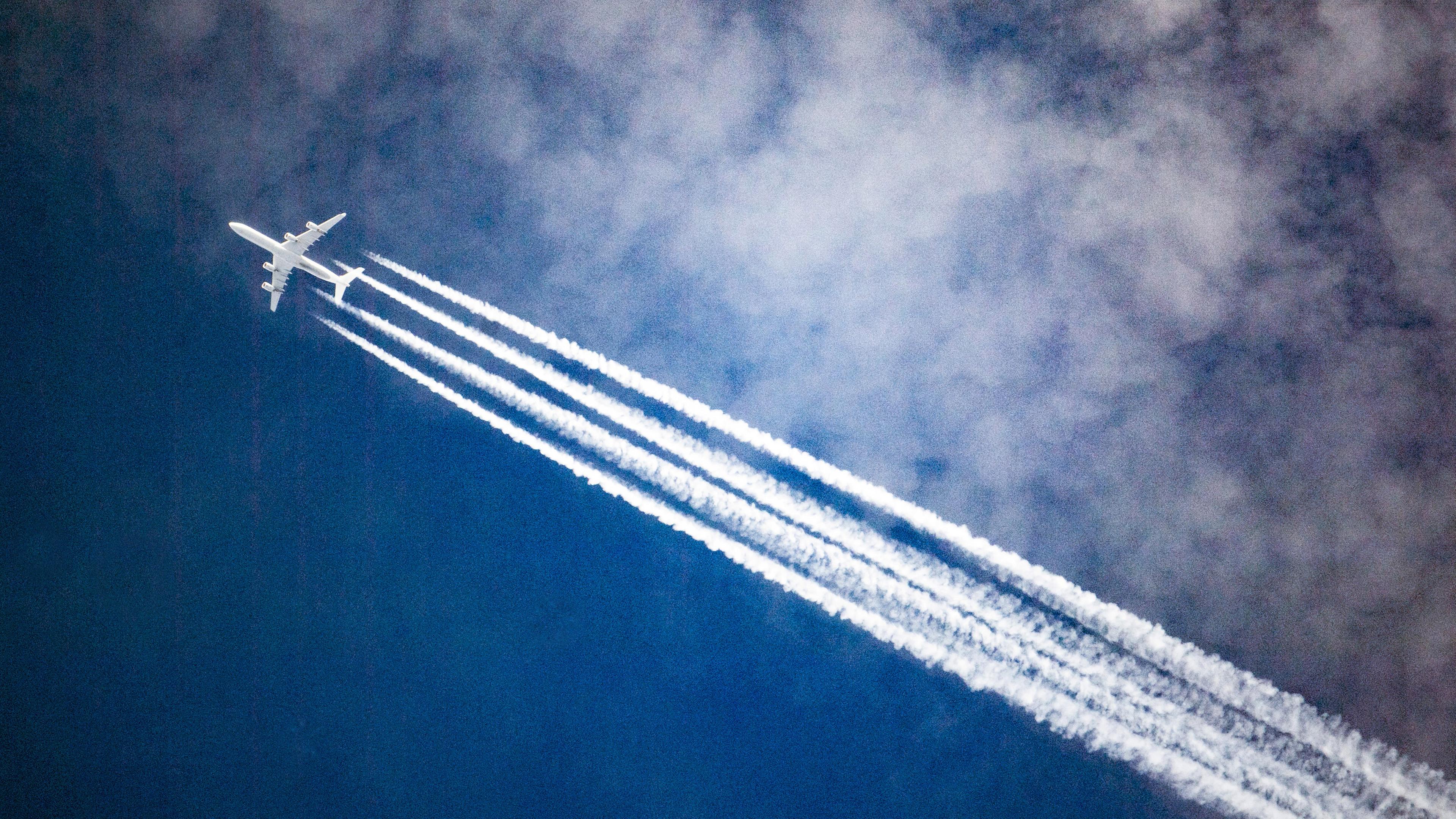 Ein Flugzeug zieht Kondensstreifen hinter sich her, waehrend es durch die Wolken fliegt.