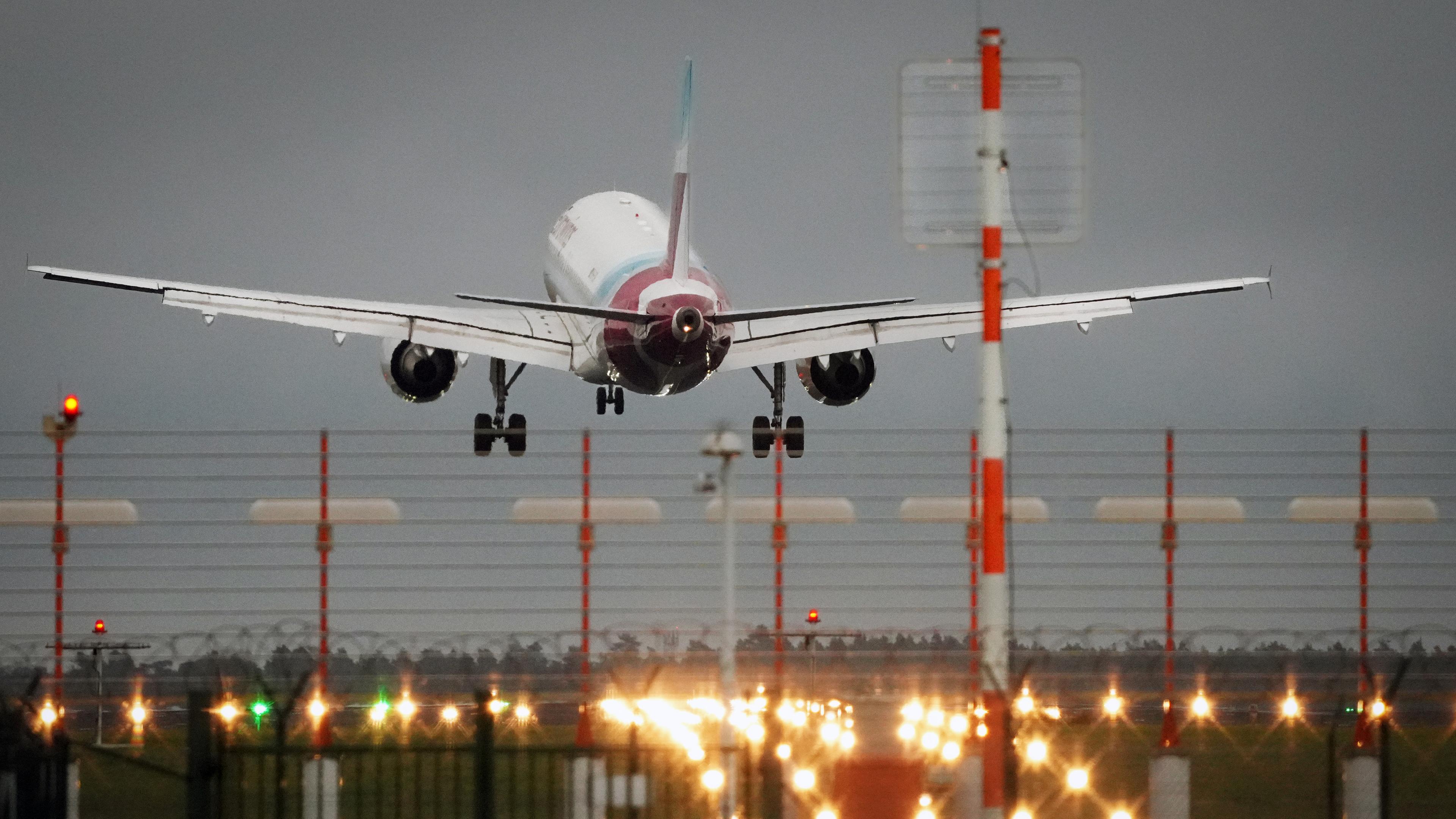 Ein Passagierflugzeug landet abends auf einer beleuchteten Startbahn.