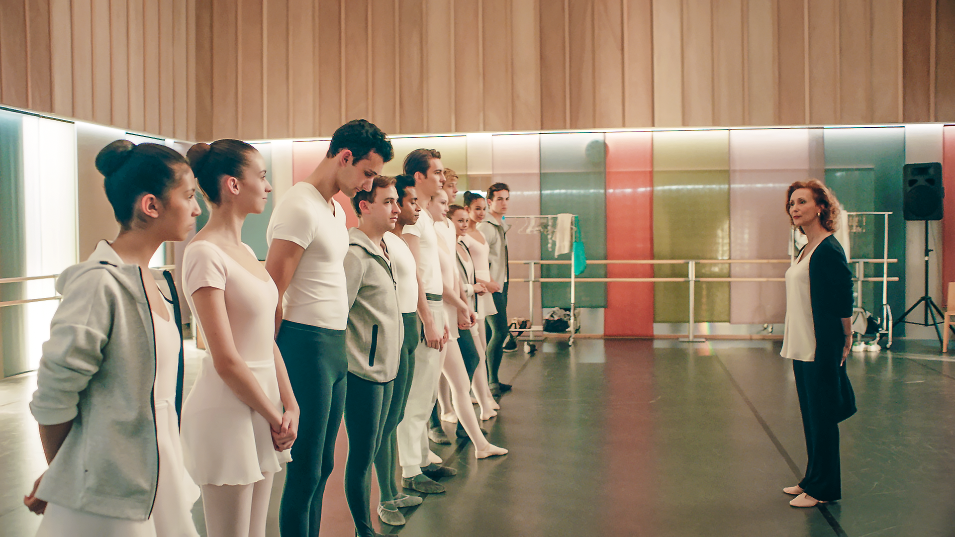 Eine Gruppe von Tänzern steht aufgereiht in einem Ballettstudio vor der Lehrerin.