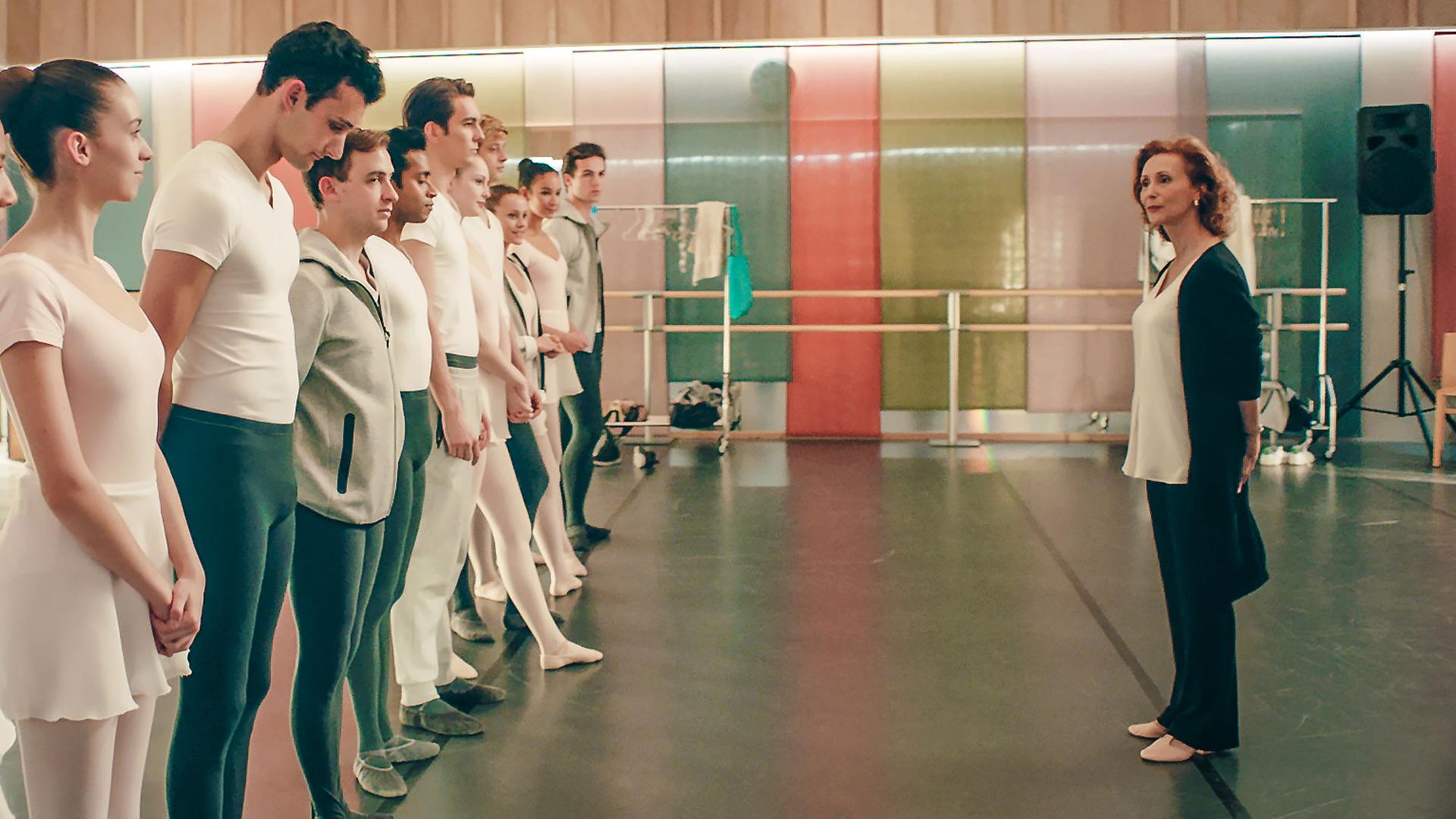 Eine Gruppe von Tänzern steht aufgereiht in einem Ballettstudio vor der Lehrerin.