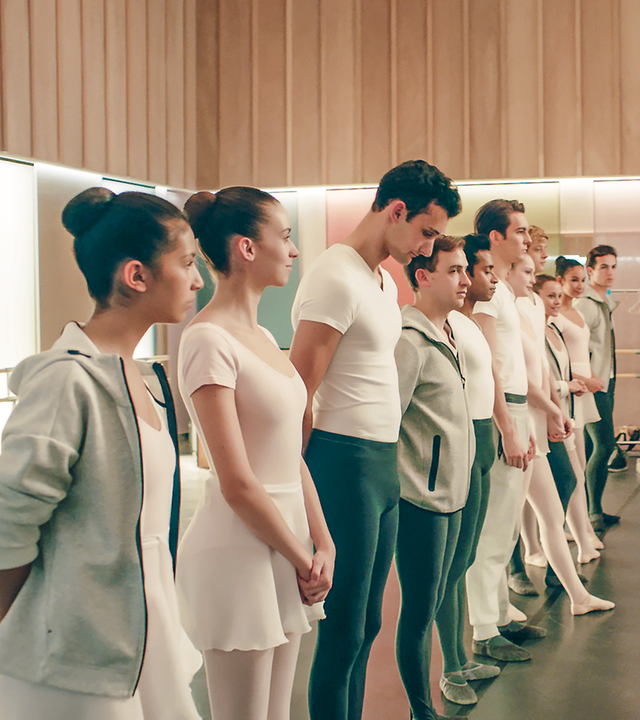 Eine Gruppe von Tänzern steht aufgereiht in einem Ballettstudio vor der Lehrerin.
