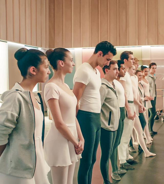 Eine Gruppe von Tänzern steht aufgereiht in einem Ballettstudio vor der Lehrerin.