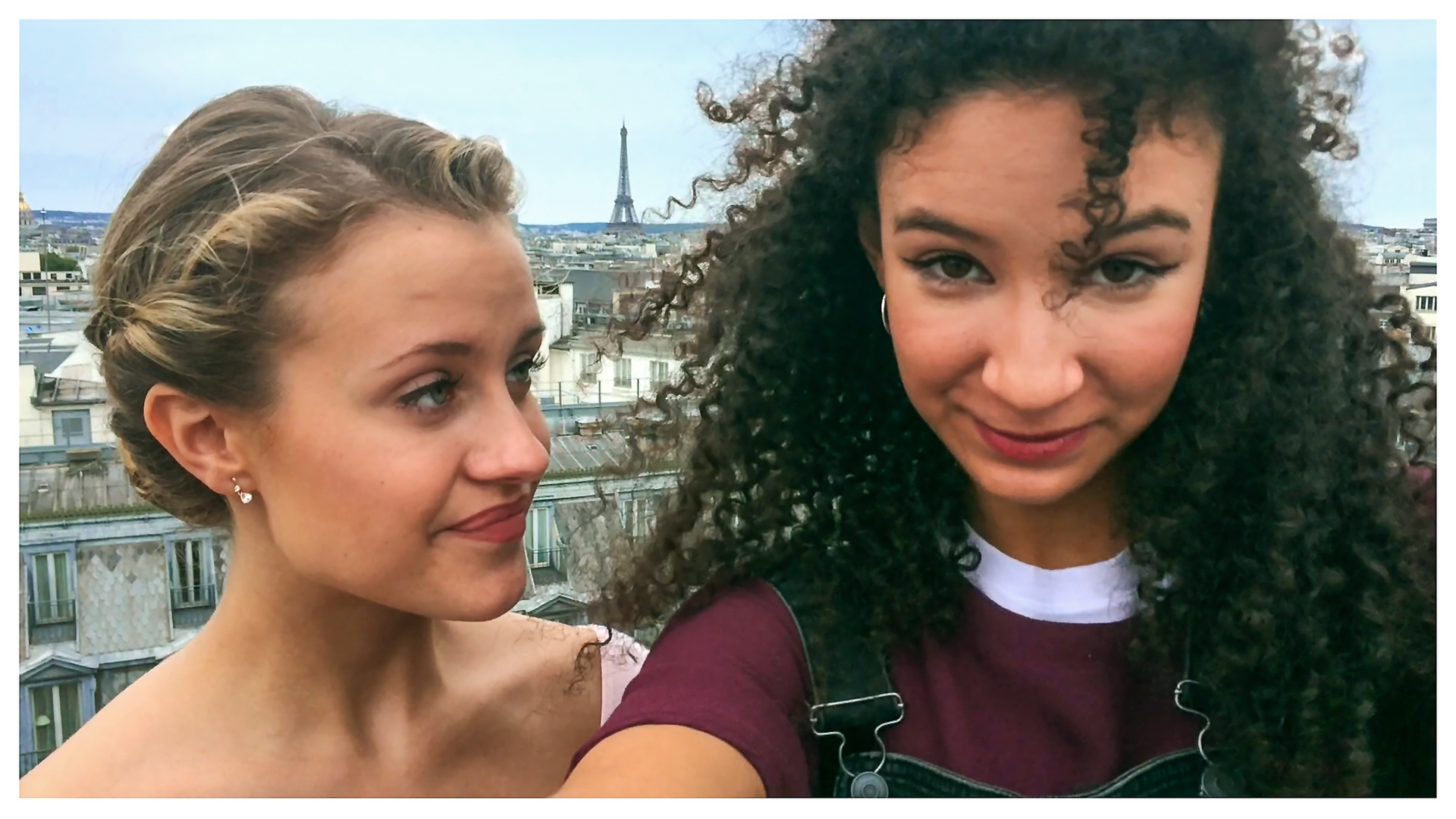 Lena steht neben Ines und schaut sie an. Sie stehen beide auf einem Dach und schauen in die Kamera.