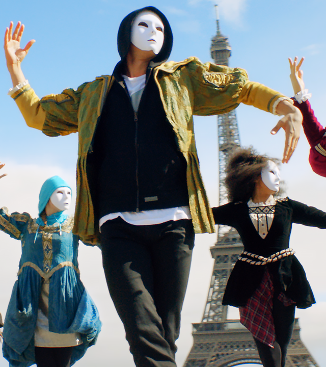 Tänzer mit weißen Masken vor der Gesicht tanzen vor dem Eiffelturm.