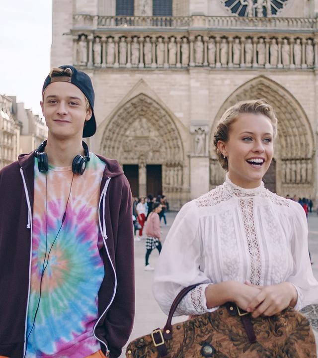 Lena läuft mit Jeff durch die Stadt. Beide haben ein Lächeln auf den Lippen. Im Hintergrund ist die Notre Dame zu sehen.