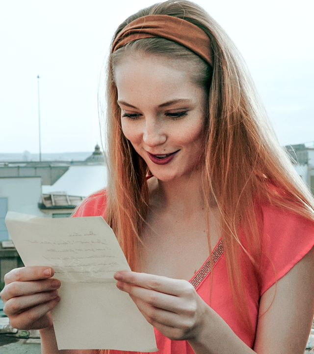 Thea hält einen Zettel in ihrer Hand. Sie liest, was darauf steht und lächelt.