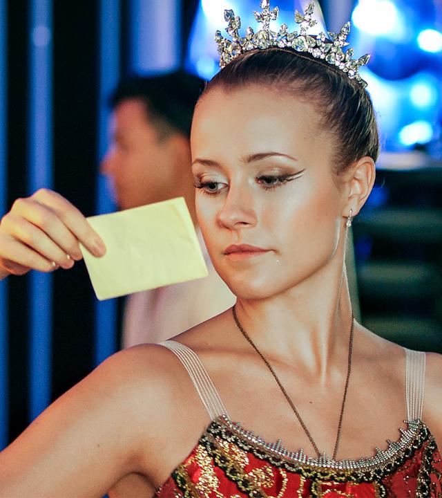 Thea zeigt Lena einen Brief. Sie haben beide sehr schöne feierliche Kleider und eine kleine Krone an.