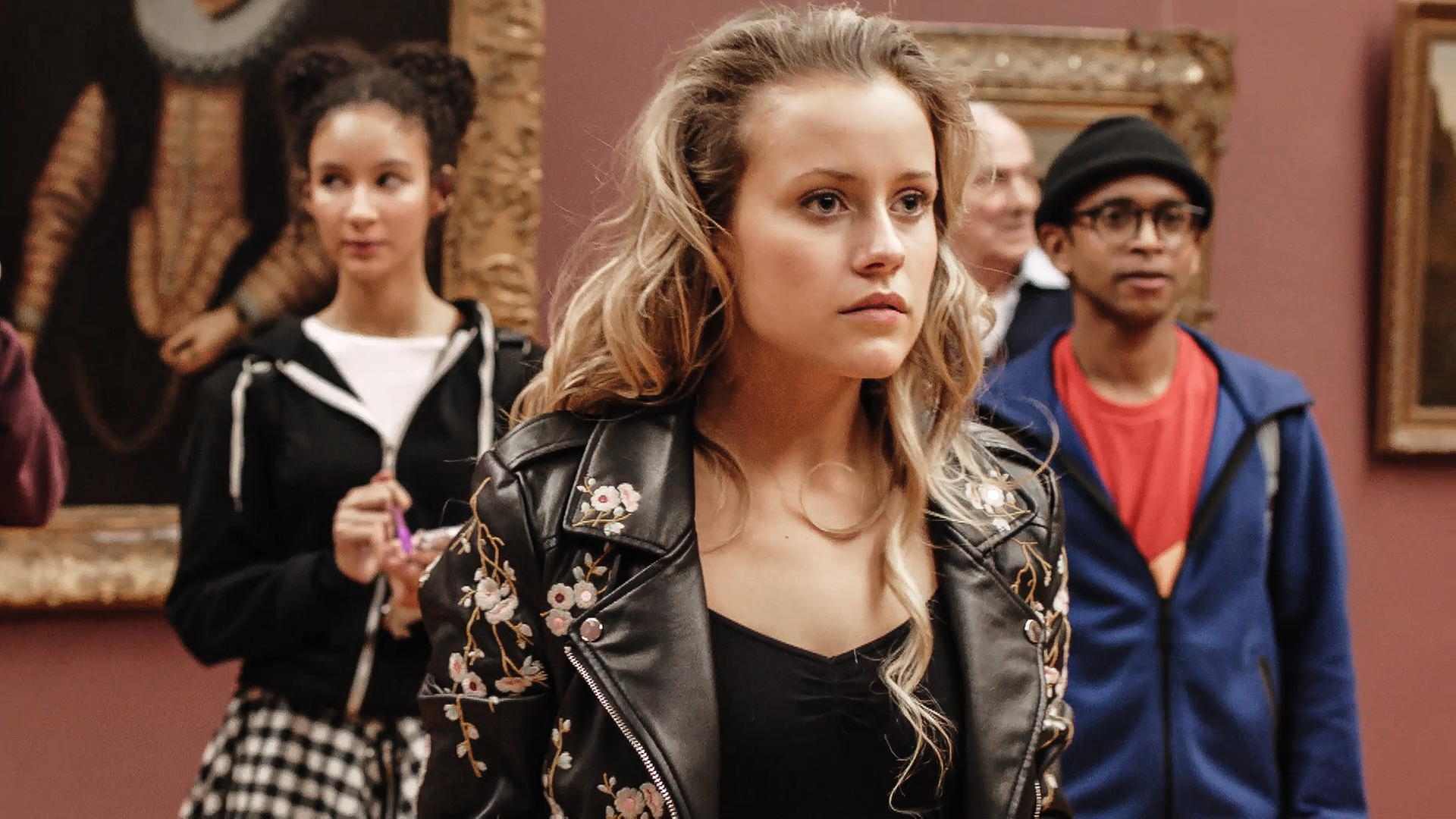 Lena steht im Museum. Hinter ihr steht Ines. Lena betrachtet etwas.