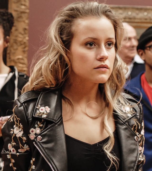 Lena steht im Museum. Hinter ihr steht Ines. Lena betrachtet etwas.