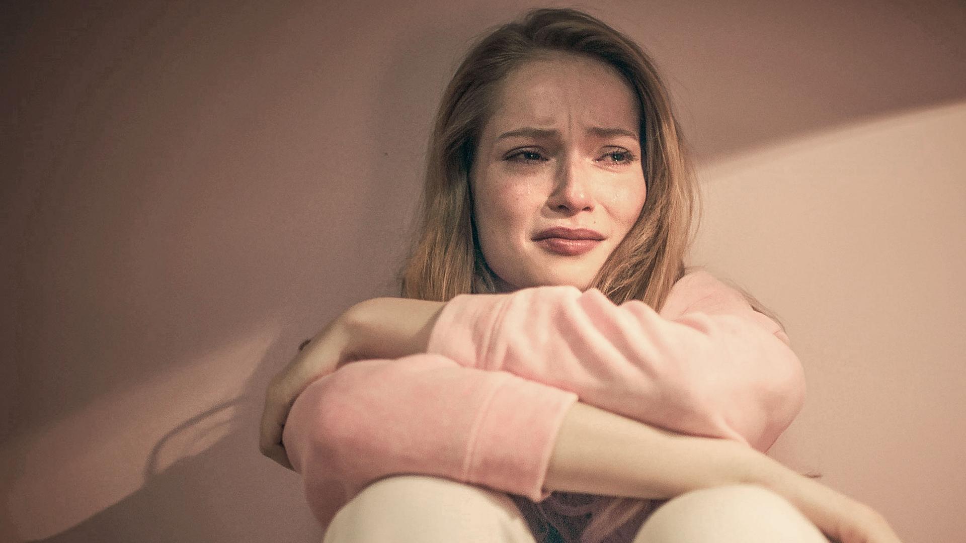 Thea sitzt weinend auf dem Boden und hat die Arme vor sich verschränkt.