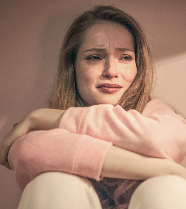 Thea sitzt weinend auf dem Boden und hat die Arme vor sich verschränkt.