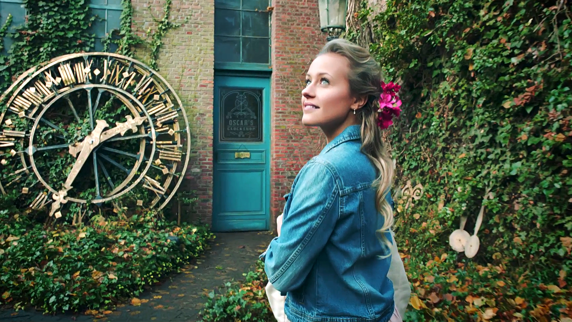 Lena blickt in den Himmel. Hinter ihr lehnt eine große goldene Uhr an einer Hauswand.