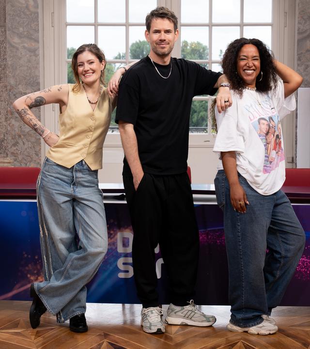 Auf dem Bild erkennt amn die neue Jury von "Dein Song": Madeline Juno, Johannes Strate und Aisha Vibes stehen in der Rotunde von Schloss Biebrich vor dem Jurypult, posieren und ächeln in die Kamera.