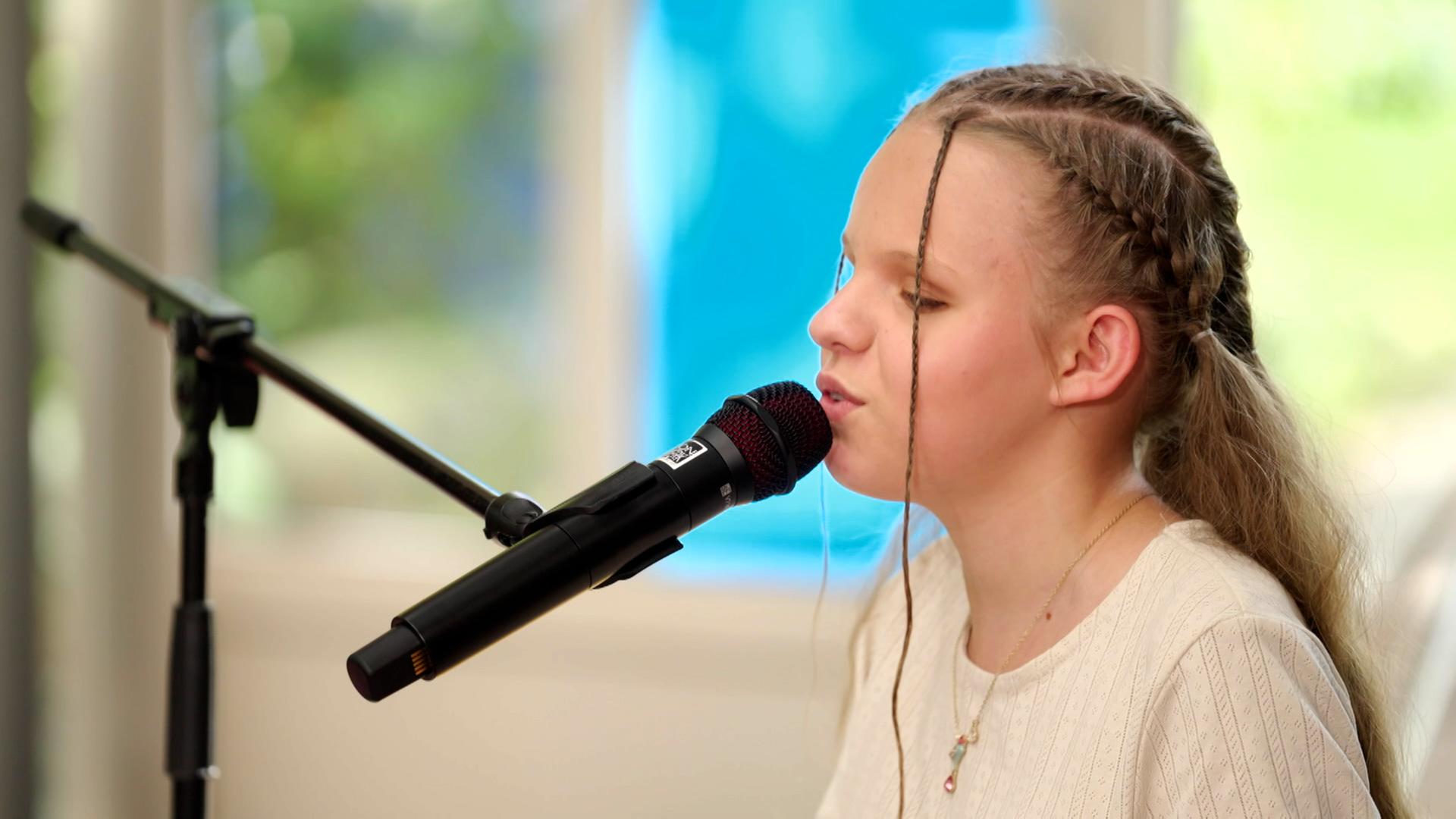 In der linekn Bildhäfte sitzt die "Dein Sond, bestehnd aus Drummer, Guitarrist, Pianist und Sängerin. In der rechten BBildhälfte ist die Kanditatin Neyla am E-Piano zu sehen. Die Momentaufnahem zeigt die Grruppe beim Performen in einem alten Gewächshaus.