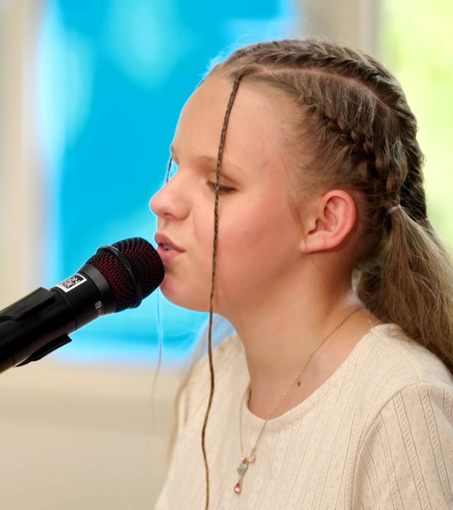 In der linekn Bildhäfte sitzt die "Dein Sond, bestehnd aus Drummer, Guitarrist, Pianist und Sängerin. In der rechten BBildhälfte ist die Kanditatin Neyla am E-Piano zu sehen. Die Momentaufnahem zeigt die Grruppe beim Performen in einem alten Gewächshaus.