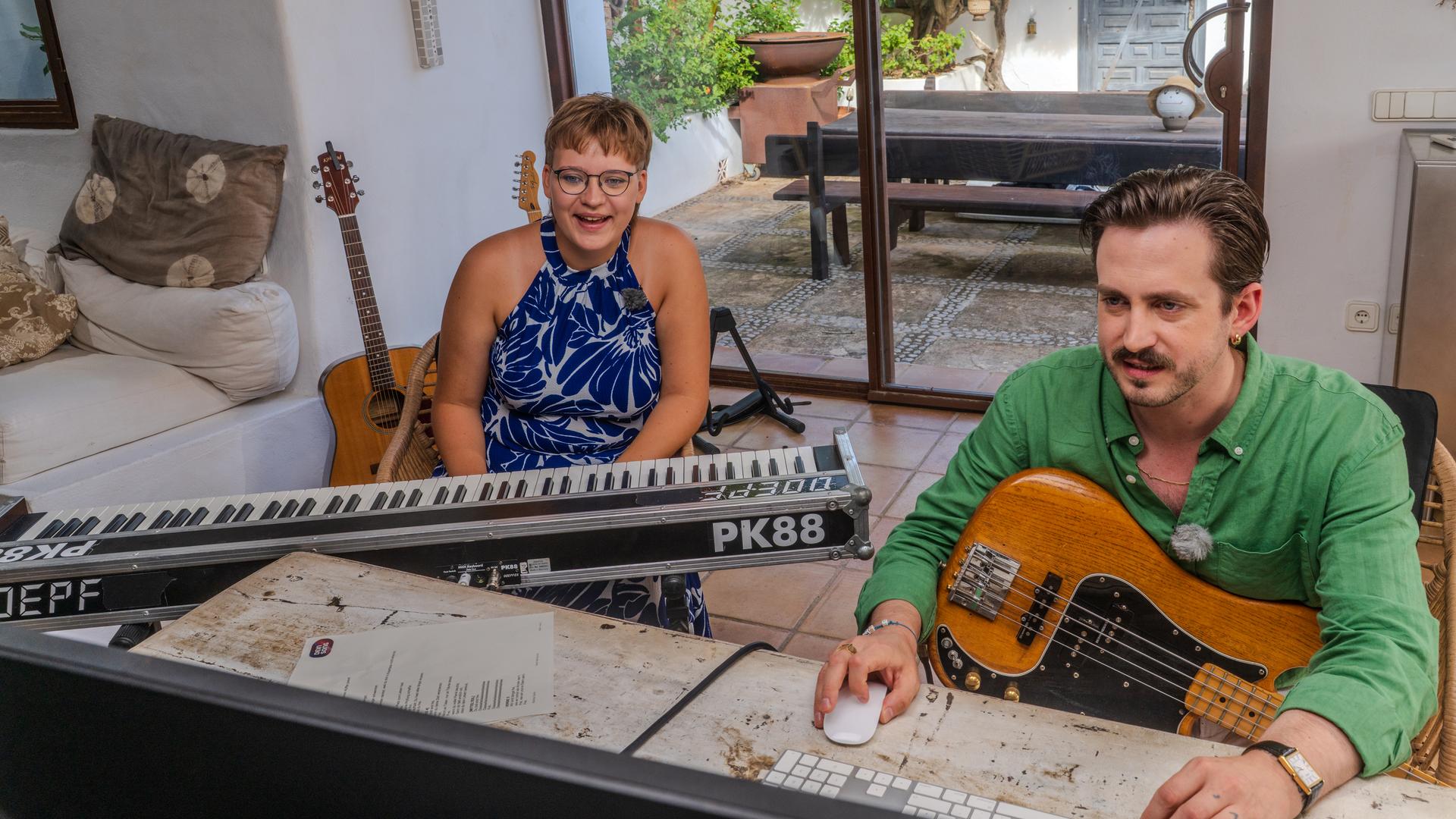Das Bild zeigt die "Dein Song"-Kandidatin Matilda mit ihrem Paten Marti Fischer (v.l.n.r.). Matilda sitz an einem E-Piano und Marti bedient mit seiner rechten Hand eine Maus während er eine E-Gitarre auf dem Schoß hat. Die beiden sitzen in einer Finca auf Ibiza.