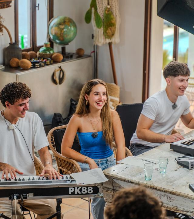 Auf dem Bild sieht man den Sänger und Musikpaten Levents Geiger und das Geschwister-Duo Rina und Aki (v.l.n.r.). Aki und Levent sitzen beide jeweils an einem E-Piano. Alle drei schauen lächelnd in die rechte Bildhälfte.