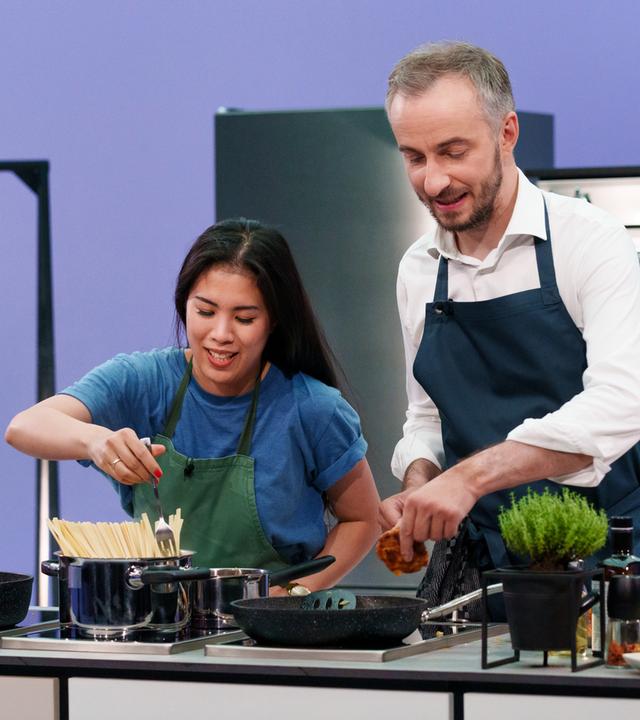 Böhmi brutzelt - Folge 04 mit Mai Thi Nguyen-Kim und Jan Böhmermann, der Kochtalk bei ZDFneo. Beide stehen in Schürze hinter einem Herd.