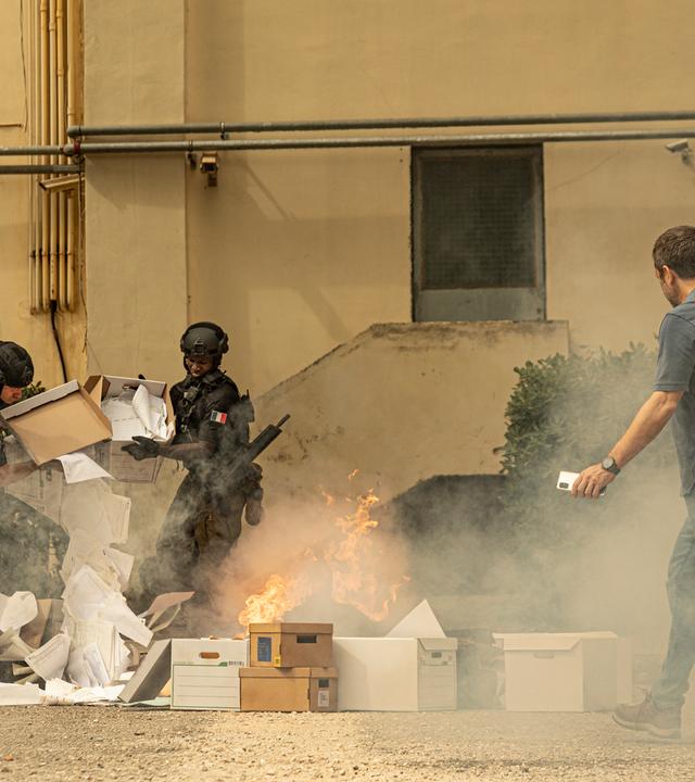 Männer in französischen Militäruniformen verbrennen Unterlagen vor einem Gebäude.