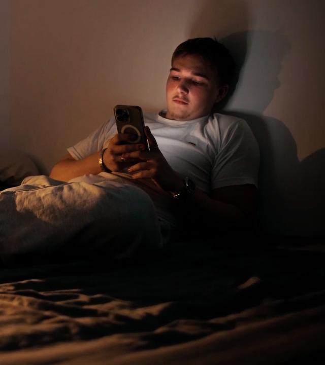 Merlin (17) liegt auf seinem Bett und schaut auf sein Handy.