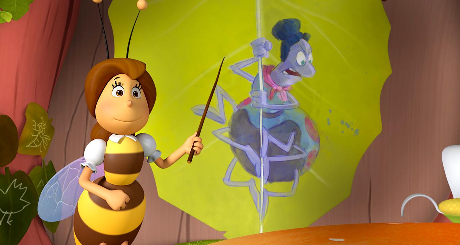 Die Lehrerin zeigt mit ihrem Zeigestock auf eine Abbildung von Spinne Thekla, die fluchend an einem Spinnenfaden hängt.