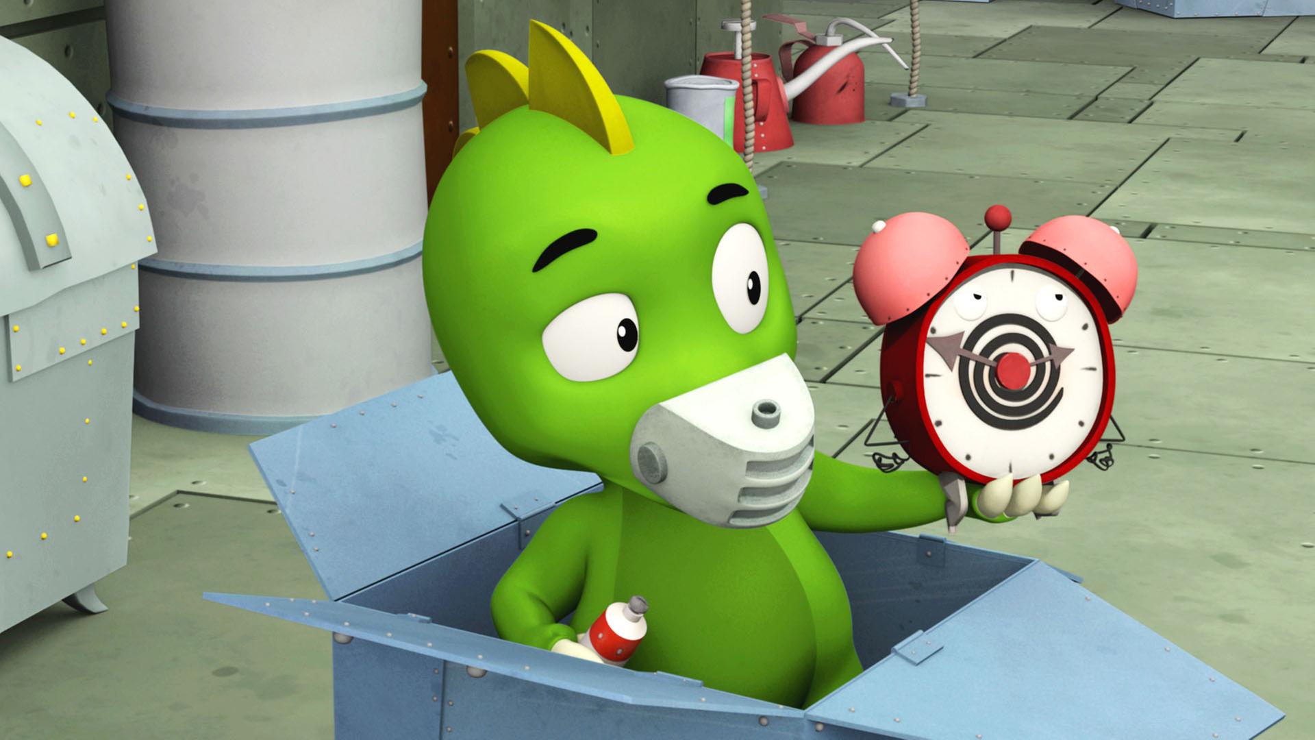 Koks steht in einem Pappkarton und hält einen Wecker in der Hand.